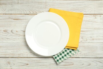 Wall Mural - Yellow and checkered napkins with empty plate on light wooden table, top view