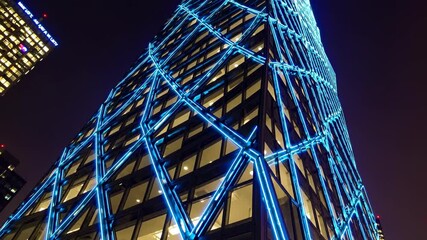 Poster - Modern skyscraper illuminated at night with striking blue lighting in an urban city setting