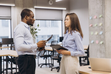 Wall Mural - Businessman and businesswoman engaging in a work discussion in a modern office, utilizing a tablet and clipboard for effective collaboration