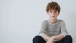 © The 2R Artificiality - Handsome young boy with curly brown hair wearing a striped long-sleeve shirt seated on a minimalistic white background, showcasing thoughtful expression.