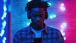 © The 2R Artificiality - Young man enjoying music through headphones, focused on smartphone, illuminated by colorful blue and pink lights in modern urban setting, deep concentration.