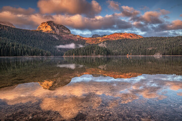 Wall Mural - Calm water reflecting colorful clouds and mountains during sunrise in Black Lake, Durmitor National Park, Montenegro