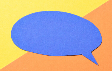 Poster - Blue blank cut out paper speech bubble with copy space for text on yellow orange background, flat lay top view conceptual backdrop