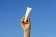 © Daryna  - Female hand holding a white thin mockup tube of cream or serum on a blue sky background. Concept of moisturizing cosmetics for face and under eyes, beauty care