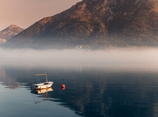 Wall Mural - Small boat floating on calm water with misty mountains in background at sunrise