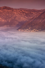 Wall Mural - Scenic view of Perast village partially covered by fog at sunrise, with its characteristic red roofs and church bell towers, located in the bay of Kotor, Montenegro