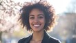 © The 2R Artificiality - Cheerful young woman with curly hair smiling joyfully outdoors surrounded by blooming trees on a sunny spring day