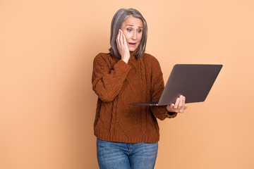 Wall Mural - Stylish mature woman looking surprised with laptop against beige background