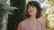 © The 2R Artificiality - Woman in dusty pink top with wavy hair, standing outdoors in a serene environment, surrounded by greenery and soft sunlight, exuding calmness and contemplation.