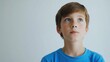 © The 2R Artificiality - Contemplative young boy with light brown hair wearing a vibrant blue shirt gazing upward against a soft white background, evoking introspection and curiosity.