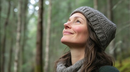 Poster - smiling middle-aged woman wearing cozy knit hat and scarf daydreaming in lush green forest with soft
