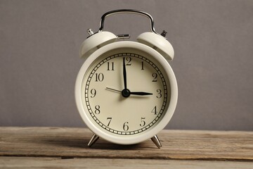 One white alarm clock on wooden table against grey background