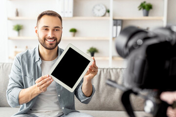 Poster - Positive male vlogger recording video review of tablet computer at home, mockup. Happy blogger showing electronic device with empty screen at camera, promoting new model of gadget