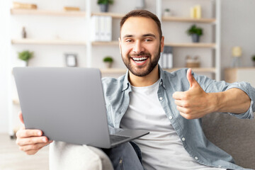 Poster - Excited millennial guy using laptop at home, showing thumb up gesture, recommending online work or studies. Young male freelancer communicating on web, taking part in business meeting