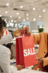 Aufkleber - Male consumer passing red sale shopping bags to shop assistant before after choosing and trying new attire in boutique