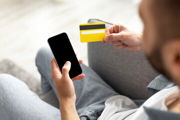 Poster - Ordering goods online. Unrecognizable young guy with credit card and smartphone shopping on web at home, mockup. Closeup of millennial man purchasing products in internet, using new mobile app