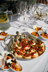 Beautifully arranged table with appetizers, including bread topped with caramelized onions and greens, white dishes with pastries, a pitcher of water with lemon and mint, and empty champagne flutes