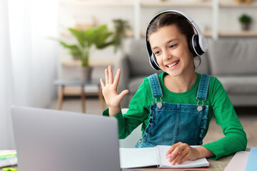 Poster - Distance Learning. Cute teenage girl in headset having video lesson using laptop in living room, studying remotely, enjoying online education, waving hand at pc web camera