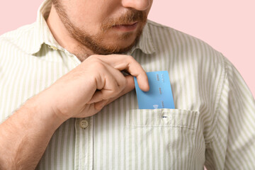 Wall Mural - Young man putting credit card in shirt pocket on pink background, closeup