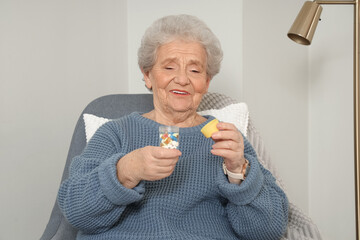 Poster - Senior woman with pill bottle sitting in armchair at home