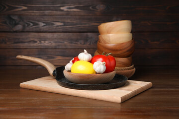 Wall Mural - Bowls, frying pan with vegetables and lemon on wooden table. Cooking utensils