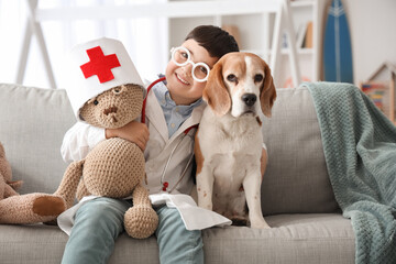 Poster - Cute little doctor with Beagle dog and toy bear sitting on sofa at home