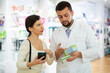 © JackF - Friendly man pharmacist helping young adult woman with electronic prescription in her phone choosing medical supplies at drugstore