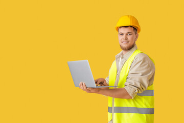 Wall Mural - male contractor using laptop on yellow background