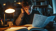 © Infinity Lens - Stressed male teenage student, exhausted and frustrated young man sitting at a desk or table in his room, holding a pen and studying. light coming from the lamp, paper notebooks open,homework deadline