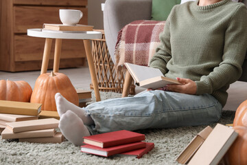 Wall Mural - Woman with pumpkins reading book on carpet at home