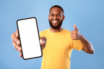 Poster - New cool mobile app. Funky African American guy demonstrating cellphone with empty screen, showing thumb up gesture, recommending website, offering space for advertisement on blue background, mockup