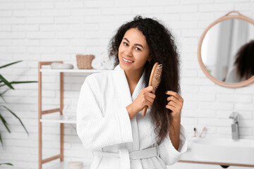 Wall Mural - Beautiful young happy African-American woman brushing her curly healthy hair in bathroom