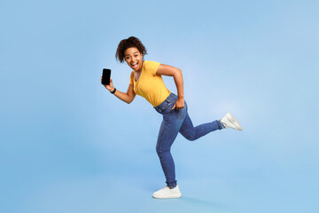 Poster - Hurry, big online sale. Happy young African American woman with empty smartphone running on blue studio background, mockup for web store website or mobile app. Space for your advertisement template