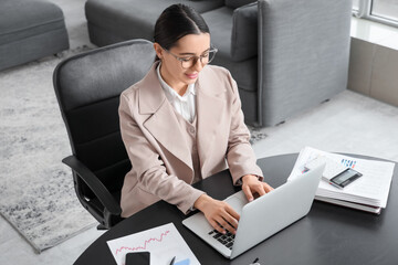 Wall Mural - Young businesswoman with laptop working on report at table in office