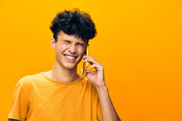 Young man smiling on the phone against a vibrant yellow background, expressing joy and excitement in a casual setting Cheerful emotions captured in a bright environment