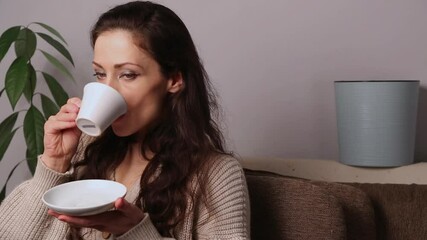 Sticker - Beautiful long brown hair happy smiling woman drinking coffee with enjoying face sitting on the sofa at home interior. Closeup lifistyle casual natural emotional video