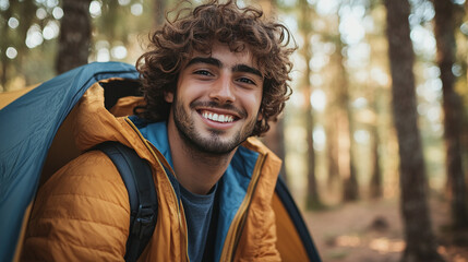 Wall Mural - Handsome young man with curly hair camping in the forest wilderness, sitting in a camp tent, smiling and looking at the camera. enjoying morning sunshine in the woods, happy female camper waking up.