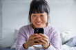 © Jovo Jovanovic/Stocksy - Smiling woman using smart phone on bed at home