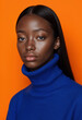 © Usama - Closeup portrait of a young Black woman with long dark hair, wearing a royal blue turtleneck sweater against a vibrant orange backdrop. Her expression is serious and direct.