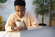 © Jimena Roquero/Stocksy - young man drinking tea while using laptop in bright office