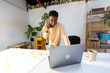 © Jimena Roquero/Stocksy - Standing smiling man in office speaking on his phone by laptop on desk