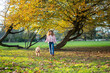 © Daniel Gonzalez/Stocksy - Woman walking with dog in autumn park under golden tree