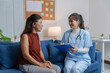 © amnaj - Female doctor holding clipboard and smiling while interviewing patient on sofa in hospital