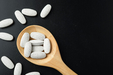 Wall Mural - white Pills Medicine tablet capsules in a wooden spoon blister pack on a black background