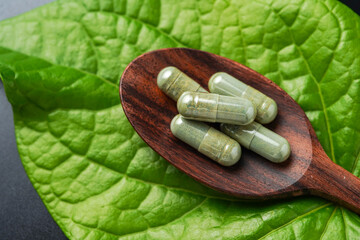 Wall Mural - Pile of herbal capsules on wooden spoon with herbs and green natural Betel pepper leaf background