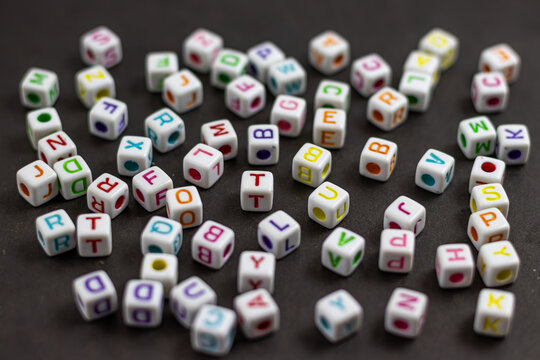 A colorful scattering of letter cubes spills across a dark surface, creating a playful and whimsical scene. The image evokes a sense of creativity and the joy of learning.