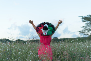 Wall Mural - Mexican woman wearing typical Mexican hat and dress, raising her arms with joy. Portrait in a country scene