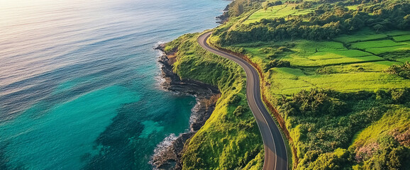 Fototapete - Aerial view of a coastal road winding along the cliffs next to the ocean with lush green hills on one side, showcasing the beauty of nature and the serene landscape.