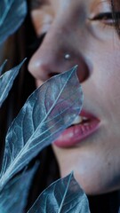 Leinwandbilder - a close-up of a woman's lips and nose partially hidden by delicate, glowing blue leaves.