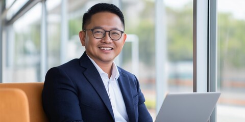 Wall Mural - A man in a suit and glasses is smiling and holding a laptop. Concept of professionalism and confidence, as the man is comfortable and at ease while working on his laptop. The combination of the suit